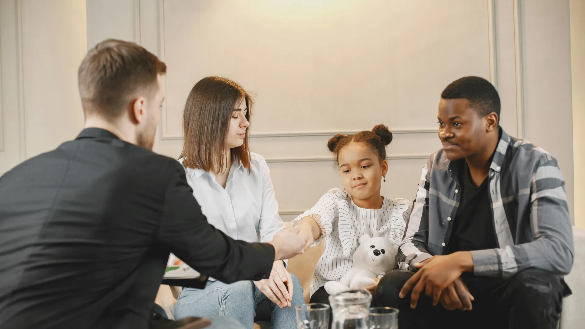 A young girl sits between her parents and is shaking hands with her specialist child counsellor.
