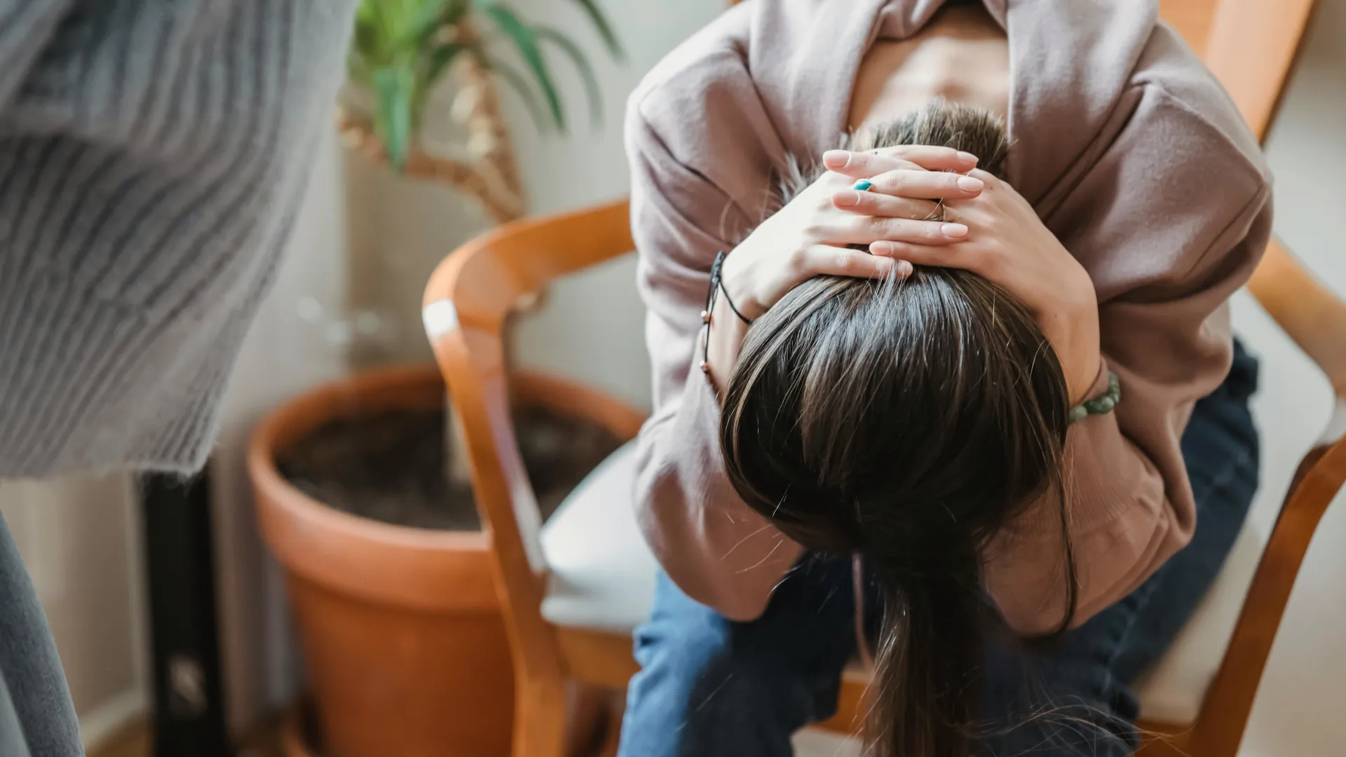 A young female has her hands clasped behind her head and her head on her knees as she is visibly tired and upset.